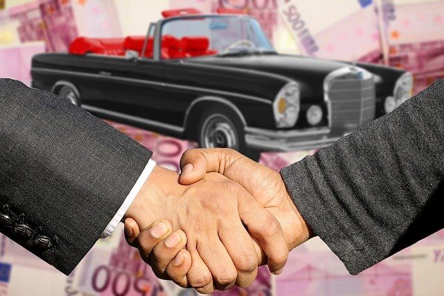 Immagine di una stretta di mano davanti a una macchina photoshoppata e denaro